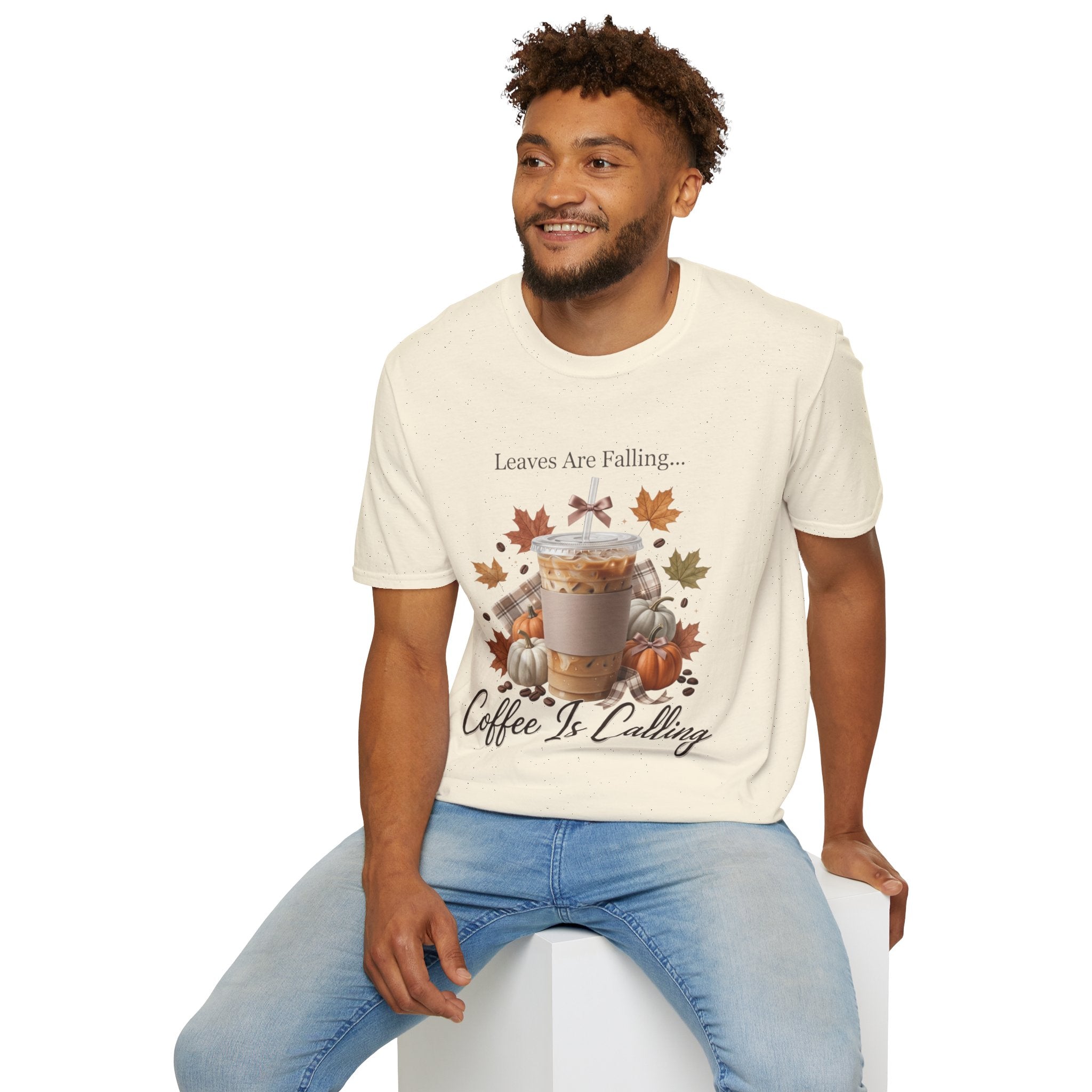 Man wearing a cream-colored "Leaves Are Falling... Coffee Is Calling" t-shirt with an iced latte, pumpkins, and autumn leaves graphic.