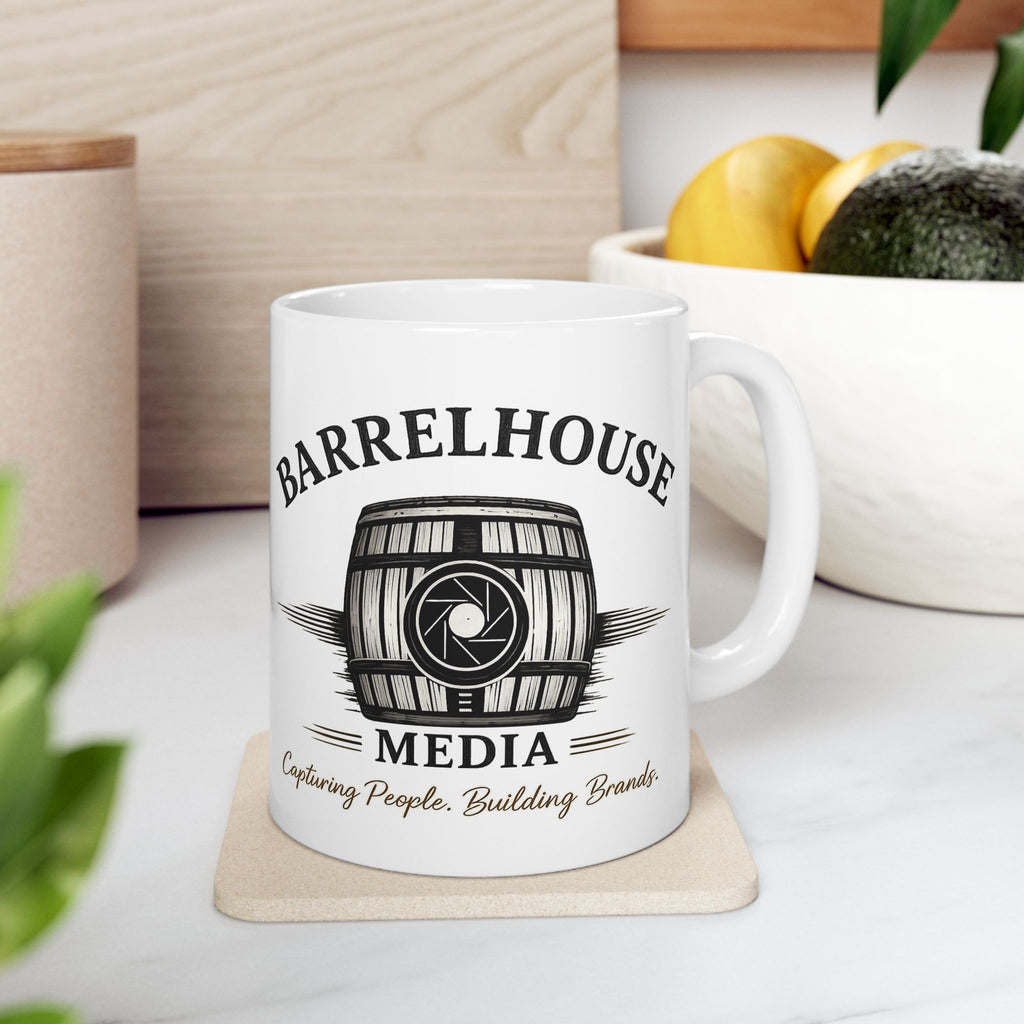 Front view of a white ceramic Barrelhouse Media Logo Coffee Mug with a barrel and camera lens graphic.